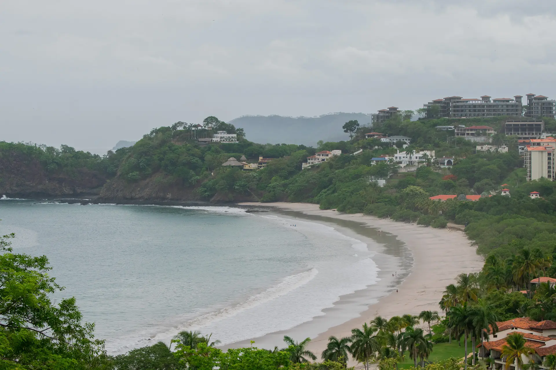 Bahía curva de arena blanca con pueblo en la colina en Playa Flamingo